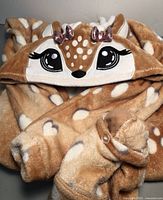 Close-up photo of the hood and upper part of brown kids deer onesie with white spots and decorative embroidered eyes and bows.