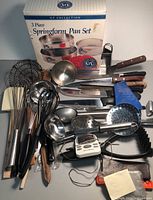Wide view showing assortment of kitchen tools including whisks, ladles, meat tenderizer, knives, digital timer, and packaging of springform pan set.