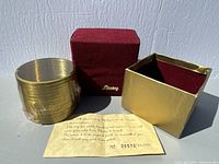 Photo showing the gold colour metal Slinky compressed and still sealed, alongside the red velvet holder and gold protective box.