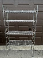 Full view of the metal shelving unit with four wire grid shelves against a brown garage door.