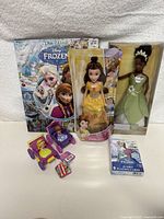 All items including Belle and Tiana dolls, Frozen Look and Find book, Frozen jumbo playing cards, and two princess carriages shown together