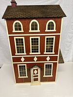 Front view of the 3-story wooden vintage doll house with brown wood finish, cream window trim and shingled roof with chimney.