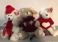 Three Ty collectible bears posed sitting against a white wall, showing entire bears and tags.