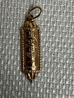 Front view of rectangular mezuzah pendant with engraved Hebrew “Shin” and Jerusalem skyline on textured background.