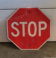 Photo of vintage red and white metal stop sign showing wear and holes for mounting.