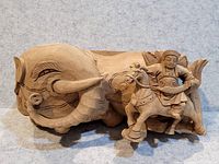 Photo of the carved wood statue showing elephant with visible tusks and detailed face, and warrior on horse in traditional attire to the side.