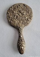 Full view of the antique hand mirror showing the embossed rose pattern on the back and its full handle.