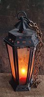 Front-side view of the antique hexagonal candle lamp lit with a visible flame inside, showing metal frame and glass panels.
