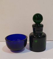 Set showing dark green glass bottle with round stopper next to deep cobalt blue glass bowl.
