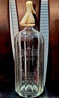 Full view of the antique soda bottle showing entire clear glass body and beige siphon.