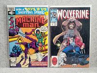 Photo of two Marvel comic books, Machine Man #50 and Wolverine #81, both in plastic protective sleeves on a neutral background.