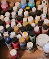 Top-down view of multiple small bottles and jars of artist paints in various colors packed in a box.