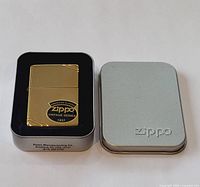 Zippo lighter displayed inside original Zippo metal tin case with the lid off and placed beside it.