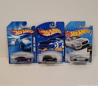 Photo showing three Hot Wheels die-cast cars in packaging with various designs and years