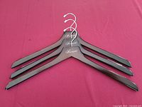 Set of three dark polished wooden hangers laid out on a red surface showing style and brand marking.