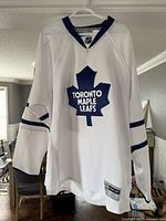 Full front view of white Toronto Maple Leafs hockey jersey on hanger, showing logo and overall design.