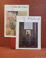 Two art books standing upright against reddish background; titles and artists visible on covers.