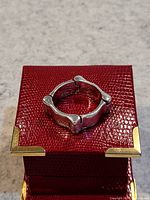 Close-up of unique sterling silver ring on a red textured box with gold corner accents, showing the ring's geometric design and bump-like details.