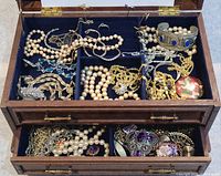 Top view of wooden jewelry box filled with various pieces of pearl bead necklaces, gold chains, rings, and decorative items.