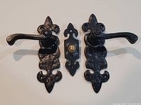 Two cast iron door handles and a doorbell push plate displayed on white background showing front detail and condition.