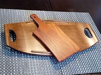 Photo of vintage teak tray with cutout handles with smaller teak cutting board resting on top, showing wood grain and condition.