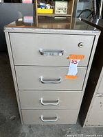 Front view of gray metal 4 drawer file cabinet with recessed handles and lock on top drawer, showing minor wear and tear.