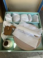 Boxed Asian dish set showing contents wrapped in protective paper including wooden chopsticks, small bowls, and serving piece.