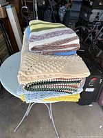 Stack of folded hand-knitted blankets and throws on a round table, showing various colors and knitting patterns.