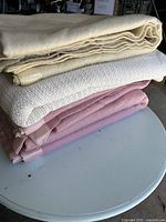 Four folded blankets stacked in cream, white, and pink colors placed on a light gray round table.