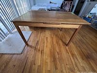 Full side angle view of the wood extendable dining table on wood flooring.