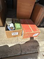 Two cardboard boxes; one marked 'assorted dishes' containing assorted dishware, the other a large box labeled as containing 24 glasses.