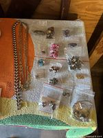 Full view of jewelry assortment with multiple chains and earrings in plastic bags on a towel