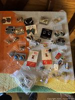 Top-down photo showing entire assortment of vintage earrings and pins laid on a cloth surface, many stored in small plastic bags