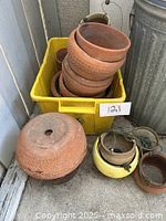 Top view of yellow bin filled with stacked terracotta pots, metal hangers, and ceramic pots seen to the sides.