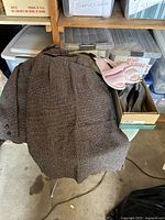 Photo of brown textured ladies suit jacket draped on chair with box nearby containing shoes and possibly a skirt or jacket