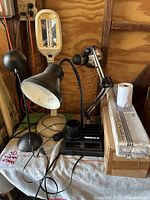 Photo showing four desk lamps of different designs including dome shade with gooseneck stems and an adjustable arm lamp with magnifier, plus two boxed wall light fixtures.