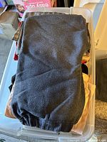 Black fleece sweatpants folded on top of a plastic bin under other clothing items