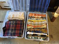 Two plastic bins filled with folded men's long-sleeve button-up shirts and t-shirts, showing a variety of colors and patterns including plaid and solid tones.