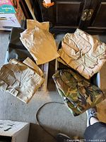 Four pieces of folded men's military clothing including camouflage jacket, tan shirts, and pants.