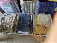 Three plastic bins filled with folded men's pants, jeans and pajama bottoms