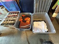 Wide view showing three plastic bins filled with men's shirts and swim trunks folded neatly. Various colors and patterns visible.