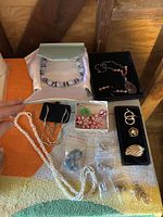 Photo showing assortment of necklaces, earrings, rings, and pins on multicolored towel with wooden background