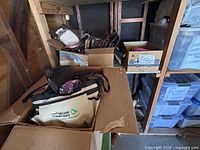 Cardboard boxes and bins containing assorted purses, bags, and wallets in various colors and sizes, placed on wood shelving in a storage area.