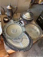 Overview of all silver and brass serving pieces, showing coffee service and trays on wooden surface.