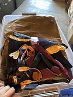 Assorted men’s suit jackets and suspenders shown inside a plastic bin, folded and stacked.