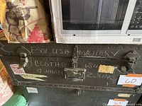 Front view of vintage army foot locker trunk with visible chalk writings and metal handle.