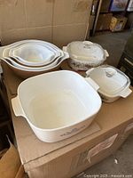Three Corning Ware casserole dishes (one square and two round), two with glass lids, and a set of four nested Pyrex bowls stacked inside each other.