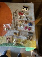 Full assortment of earrings in multiple styles and colors along with vintage chain link necklace displayed on fabric background
