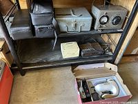 Yokoyama Electric Works LTD variable V transformer in metal case, vintage military timing light with control dials, portable radio, and accessory cases on shelf; box on floor with equipment inside.