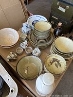 Overview of stoneware dishes, bowls, sake cups, sake bottles, and some blue/white ceramic pieces arranged on a wooden surface